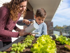 Una madre junto a su hijo regando sus plantas para huerto urbano